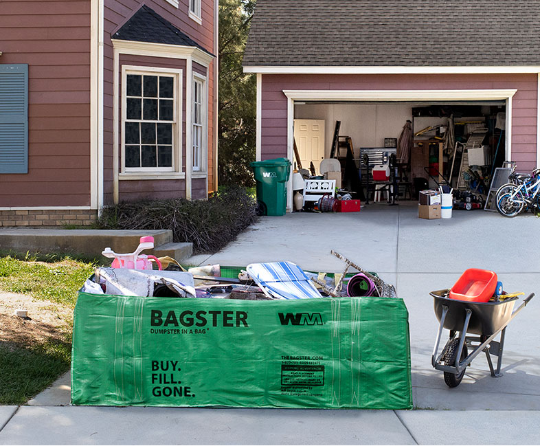 Bagster dumpster bag filled with debris from a garage cleanout and placed at the end of a driveway.