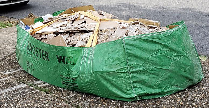 Bagster bag filled with pieces of broken drywall and placed at the end of a driveway.