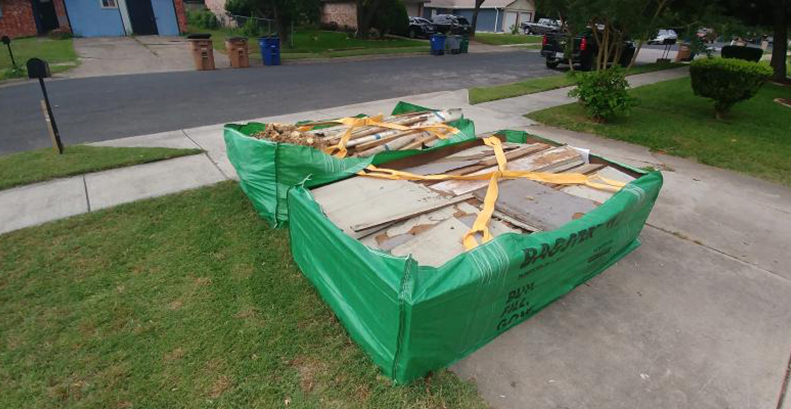 Two Bagster bags at the end of a driveway filled with drywall, subflooring, and construction materials.